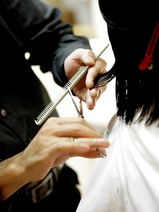 A stylist cutting dark hair with scissors, holding a comb in the same hand